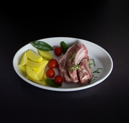 Pork ribs baked with rosemary and potatoes on white plate, top view
