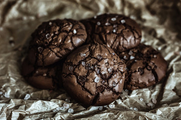 A pile of chocolate cookies with cracked tops with sea salt on craft paper