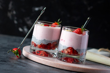 Chia seeds pudding with strawberry and banana in glasses on dark background, healthy tasty dessert....