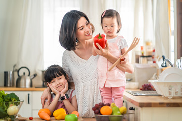 Lovely cute Asian family playing, making food in kitchen at home. Portrait of smiling mother and children standing at cooking counter that food ingredient put on table. Happy family activity together.