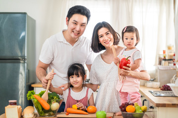Lovely cute Asian family playing, making food in kitchen at home. Portrait of smiling mother, dad and children standing at cooking counter, food ingredient put on table. Happy family activity together