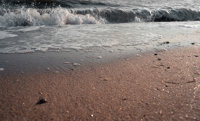 Sea wave with foam washes sand on the beach. People bathe in the water. Sea of Azov. Summer sunny day