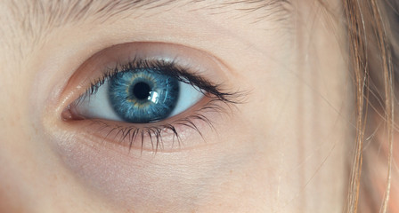A close-up of the blue eye of a white-skinned girl. Clear structure of the pupil of the eye.