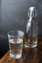 Top view of glass and glass bottle with water on dark wooden table and gray background, vertical, with copy space
