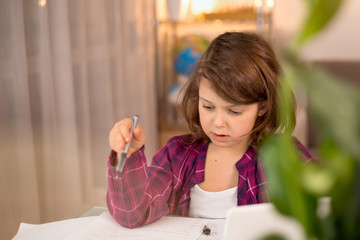 Distance learning online education. Schoolgirl studying at home with a digital mobile tablet in hand and doing school homework. Training books and notebooks on the table