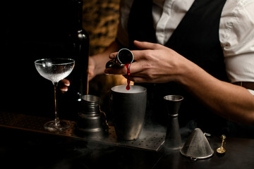 close-up male bartender pours drink from metal jigger into steel cup of shaker