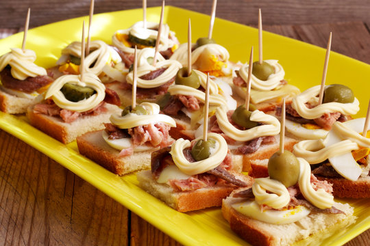Antipasto fatto in casa con stuzzichini di pane uova acciughe olive e maionese su vassoio giallo.