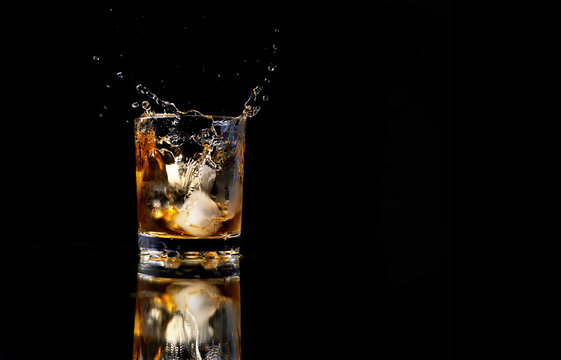 glass of whiskey with ice and a splash in reflection on a black background, whisky