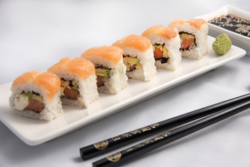 Sushi roll with pink salmon wrap, grilled salmon, Philadelphia cheese and avocado. White container and black chopsticks.