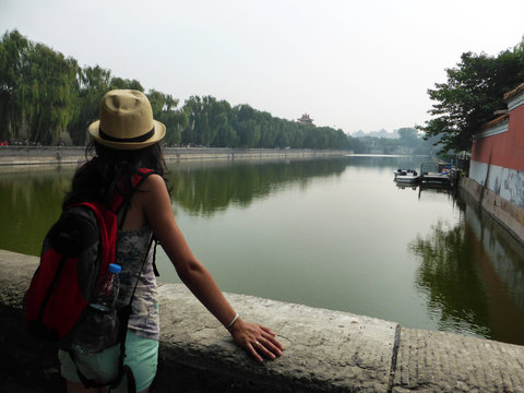 Viajera con gorro y mochila mirando el muro y foso de la Ciudad Prohibida en Beijing, China.
