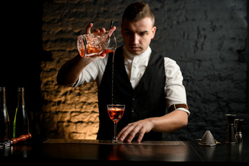 young bartender at bar carefully pours cocktail into glass