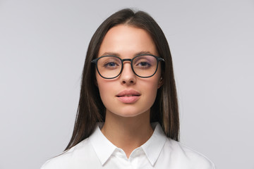 Portrait of young business woman in white collar shirt and glasses, looking straight at camera...