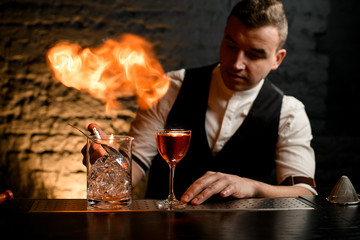 Close-up. Man at bar sprinkles on glass with cocktail and make fire.