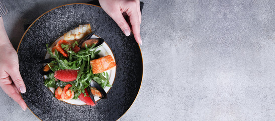 Salad with arugula and seafood on a plate with hands. Salmon, mussels, shrimp, prawn, white fish...