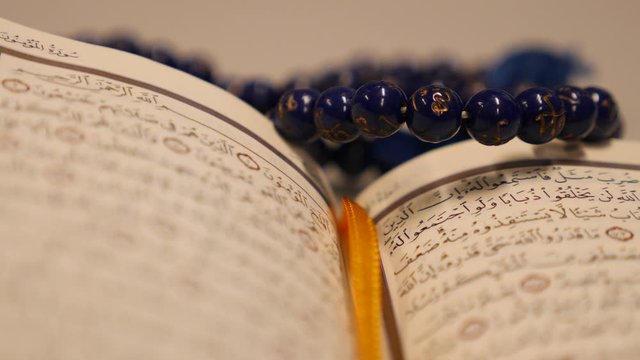 Footage of a Quran and a prayers bead near it, the shot is moving in a half circle...