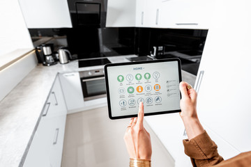 Woman controlling kitchen appliances with a digital tablet, close-up on mobile device with launched smart home application. Smart home concept