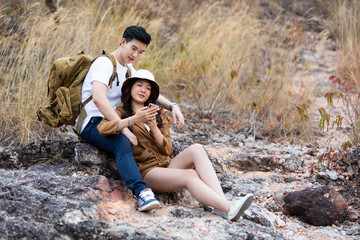 Naklejka na ściany i meble Beautiful Asian couple in love on vacation. Hikers with backpacks relaxing and enjoying view