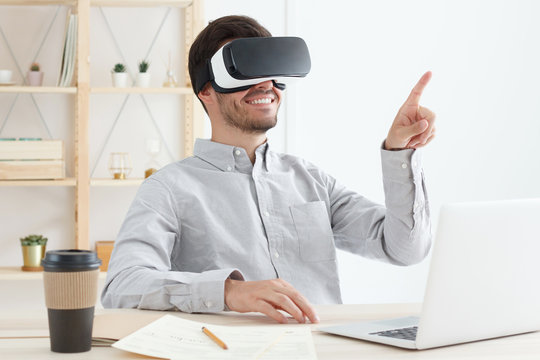 IT engineer in office enjoying his time with virtual reality headset, playing VR game and pointing finger in air, smiling happily