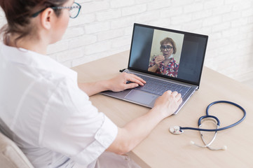 An elderly woman with the flu for an online consultation with a doctor. Female practitioner makes a video call with a patient on a laptop. A pensioner on the remote doctor's office.