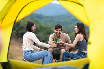 Group three Friends Camping summer concept. Group Of Friends Relaxing drinking Outside Tent and happy talk. Yellow tent is foreground.