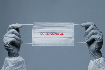 CORONAVIRUS. COVID-19 concept. medical face mask with a red inscription CORONAVIRUS in the hands of which are in rubber gloves. bleached image