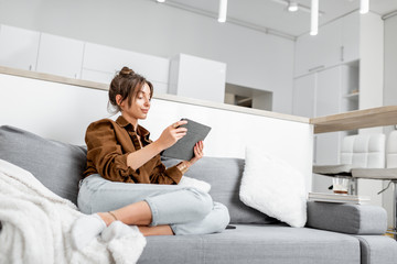 Young relaxed woman working or surfing the internet on a digital tablet while sitting on the couch at home