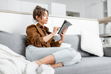 Young relaxed woman working or surfing the internet on a digital tablet while sitting on the couch...
