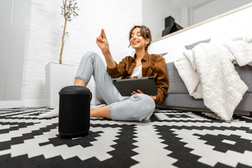 Woman using voice commands to control a smart home devices sitting with a smart speaker and tablet on the floor in the living room
