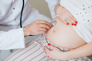 pregnancy, gynecology, medicine, health care and people concept - close up of gynecologist doctor with stethoscope listening to pregnant woman baby heartbeat at hospital