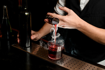 close-up. Bartender's hand masterfully pours smoky drink from jigger into glass with ice