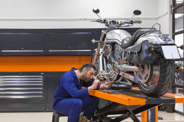 Man fixing a motorcycle raised on a lift in a modern workshop.