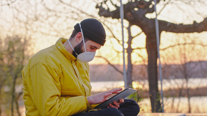 Fototapeta na wymiar In the middle of the park a guy with a protective mask stay on his tablet