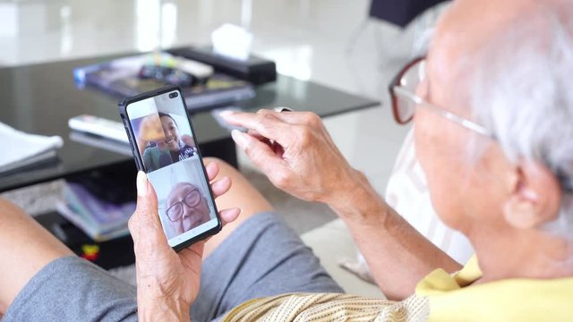 Social distancing concept. Aged man doing video chats with his grandchildren on a mobile phone during quarantine at home. Shot in 4k resolution