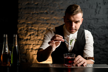 bartender accurate decorating glass with fresh green plant and look at it.