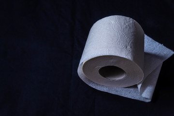 On a dark background is a single roll of white toilet paper, paper thin, single-layer, whole