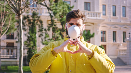 Good looking guy in the middle of the street wearing a protective mask he make a hart from hands...