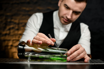 Man bartender inserts glassy tube in special designer glass flask