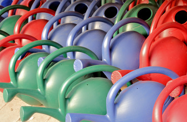Closeup of red, blue and green plastic watering cans.