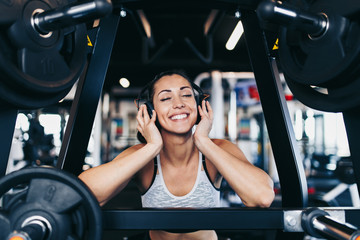 Young attractive woman after successful workout in modern fitness gym dancing, smiling and singing. She listening to music with bluetooth headset and smart phone.