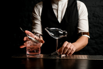 Close-up male bartender holding glass mixing cup and glass vessel in shape of bird stands nearby