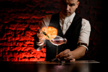 male bartender sprays and makes fire over glass vessel in shape of bird