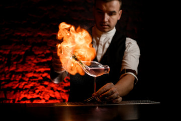 male bartender sprays and makes fire flame over glass vessel in shape of bird