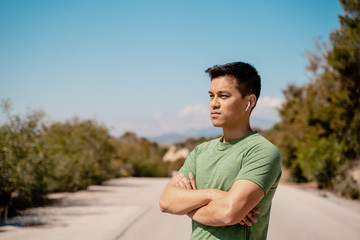 Hombre joven Asiático con brazos cruzados y con AirPods mirando hacia el horizonte, pensando con...