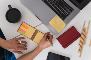 Aerial view of woman writing with a pencil on a post-it while is working