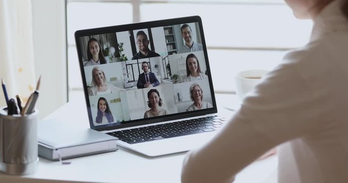 Over shoulder view of business woman remote worker, distance student video conferencing boss and colleagues by group video call using web cam on laptop screen. Virtual team home office chat meeting.