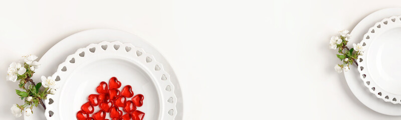 Clean empty plates on a light background. Red hearts and branch of blooming cherry on a plate. Top view. Banner.