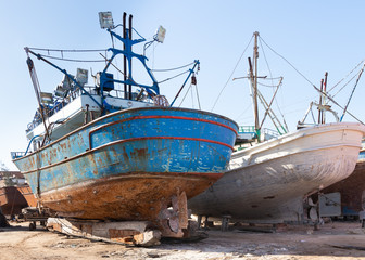 Old rusty vessels under repairing located on grungy dry dock in shipyard against blue sky on sunny day in old shipbuilding plant