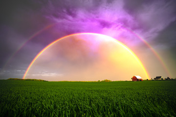 A stunning double rainbow seen in the farming prairies of the United States of America. Purple sky, vibrant landscape. 