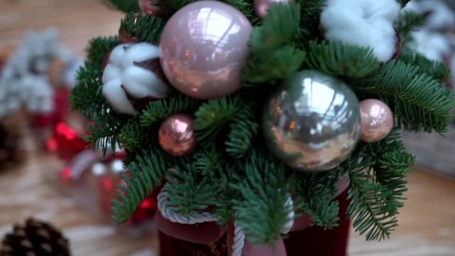 Christmas composition: pine tree branches, pink and silver christmas tree toys and cotton flower balls in gift box on plastic wrap, close-up. Craft supply for handcrafted decorations on wooden table.