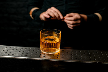 Close-up old-fashioned glass with amber alcoholic drink standing at bar counter.